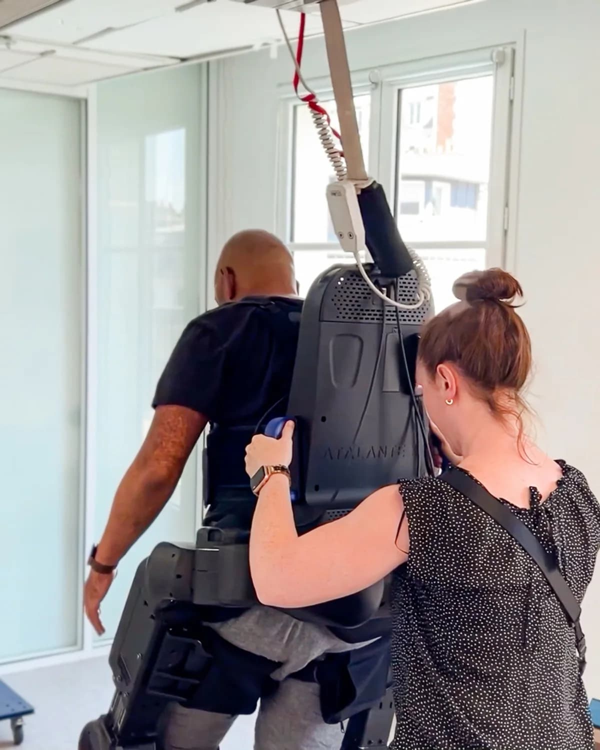 A patient walking in the Atalante X exoskeleton with a therapist supporting the session.
